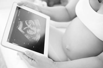 Pregnant woman looking at ultrasound of baby on tablet.